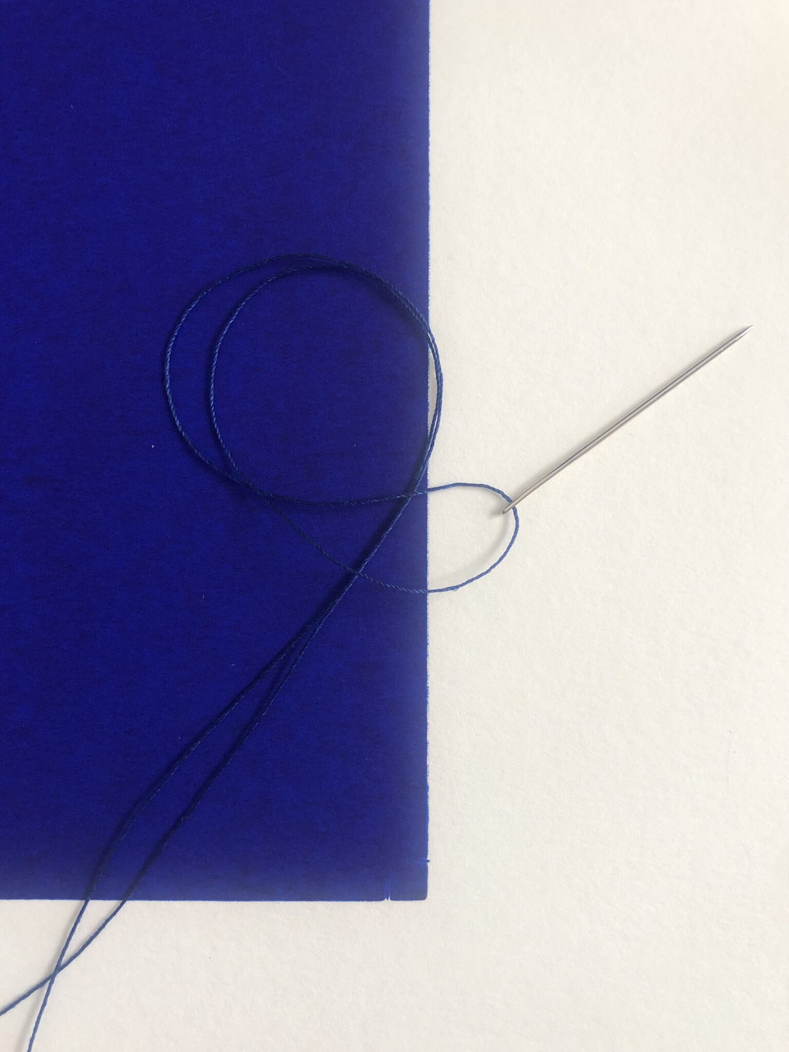 Naald en draad op een blauw blad papier.
